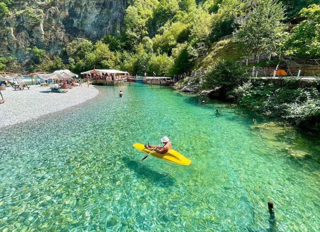 A canoe gliding through the calm waters of Shala River, surrounded by mountains and lush greenery.
