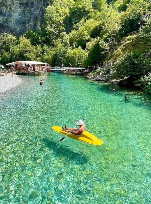 A canoe gliding through the calm waters of Shala River, surrounded by mountains and lush greenery.