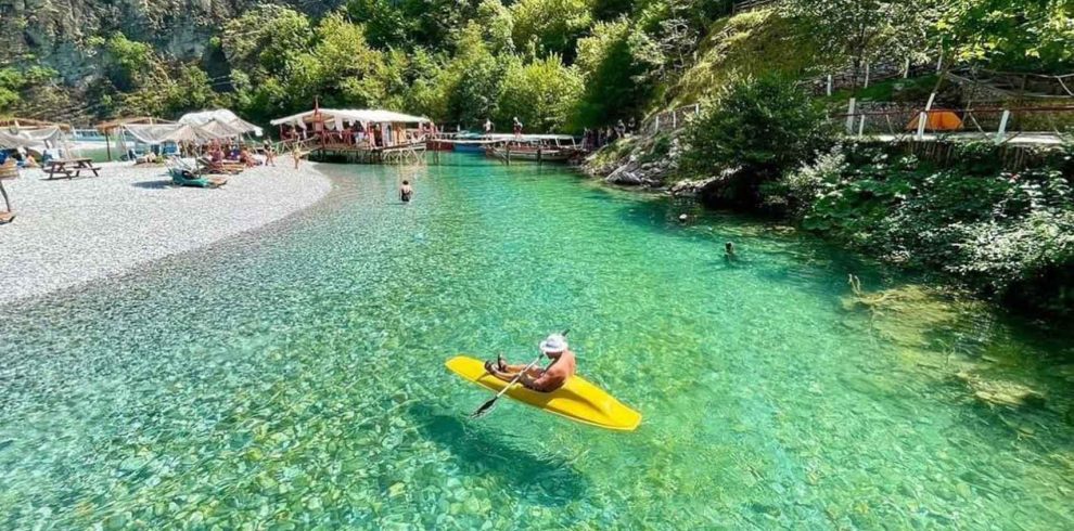 A canoe gliding through the calm waters of Shala River, surrounded by mountains and lush greenery.