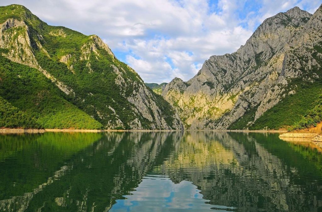 A scenic view of Komani Lake in Albania, surrounded by high green mountains and clear blue water.