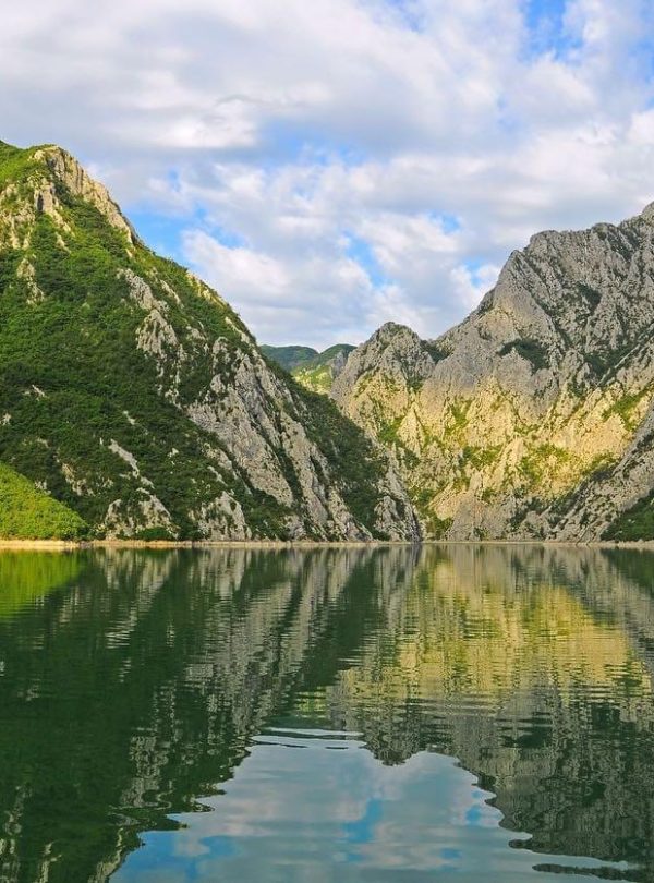 A scenic view of Komani Lake in Albania, surrounded by high green mountains and clear blue water.