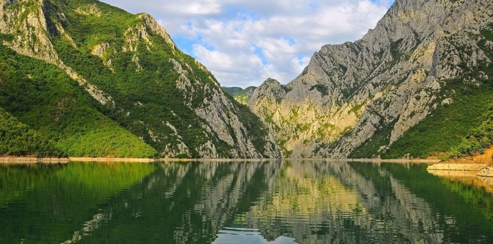 A scenic view of Komani Lake in Albania, surrounded by high green mountains and clear blue water.