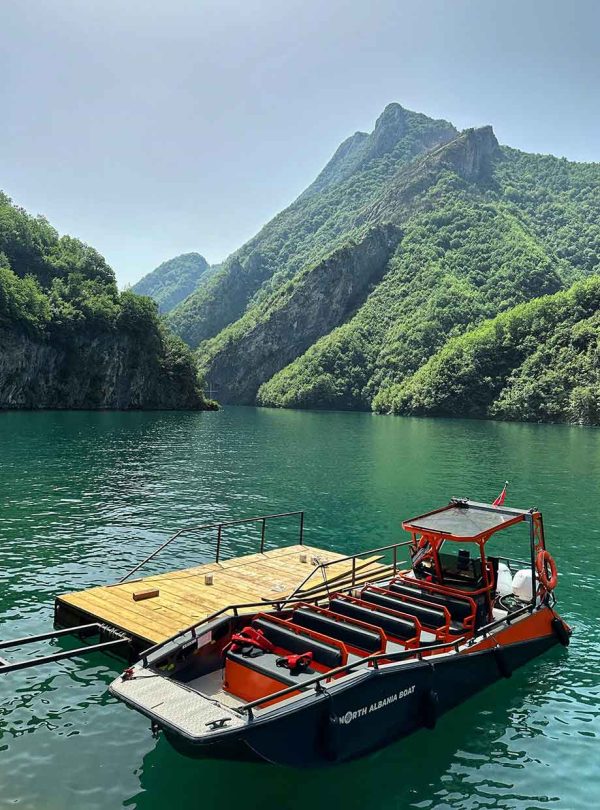 A beautiful boat on clear water, surrounded by mountains in Albania, offering a scenic tour experience.