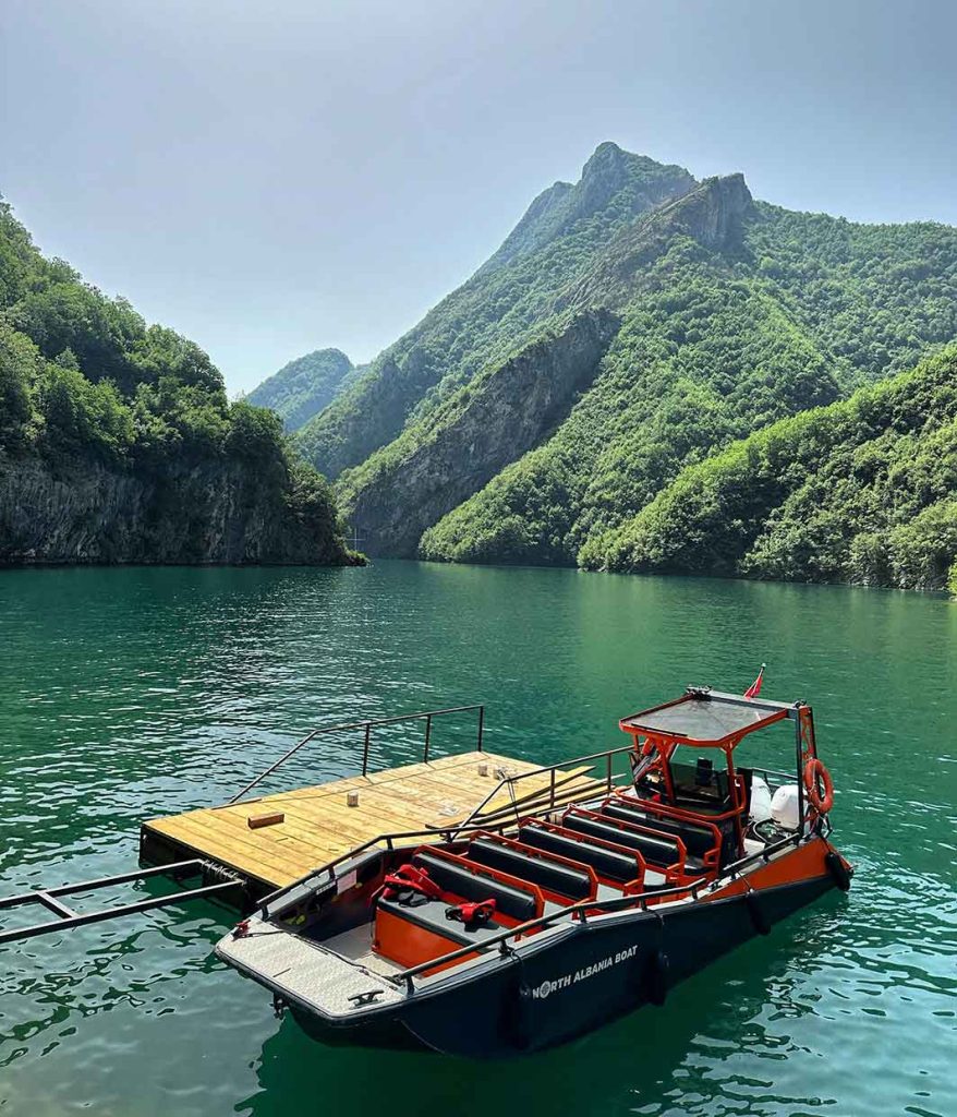 A beautiful boat on clear water, surrounded by mountains in Albania, offering a scenic tour experience.